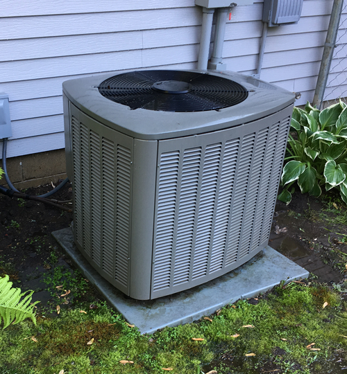 central air conditioning unit in backyard with cover off and bushes cleared around it. 