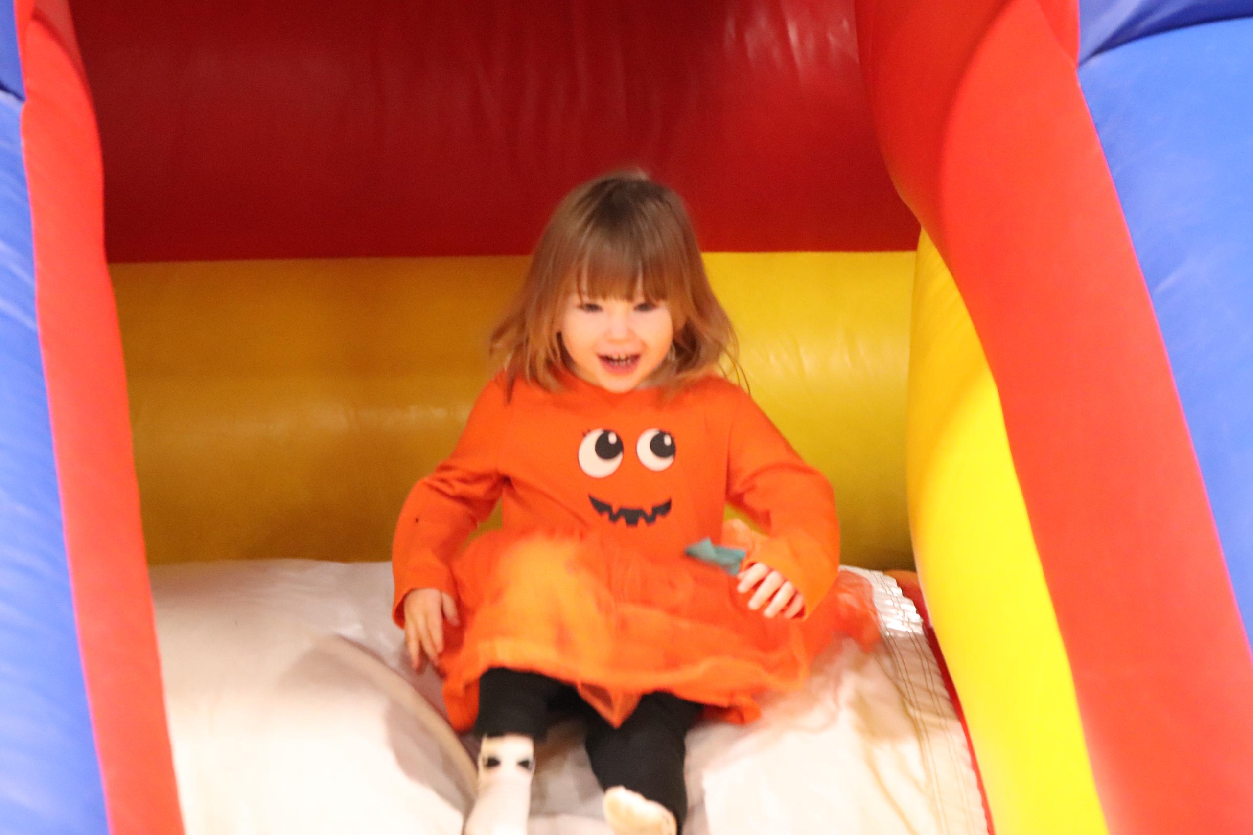 A child in a pumpkin costume goes down an inflatable slide