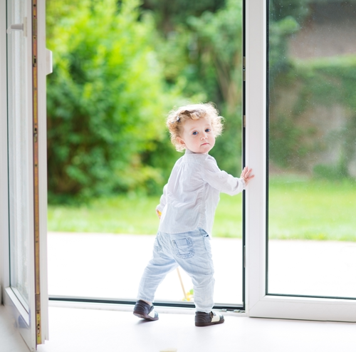 Very young girl going outside while holding open a glass door. 