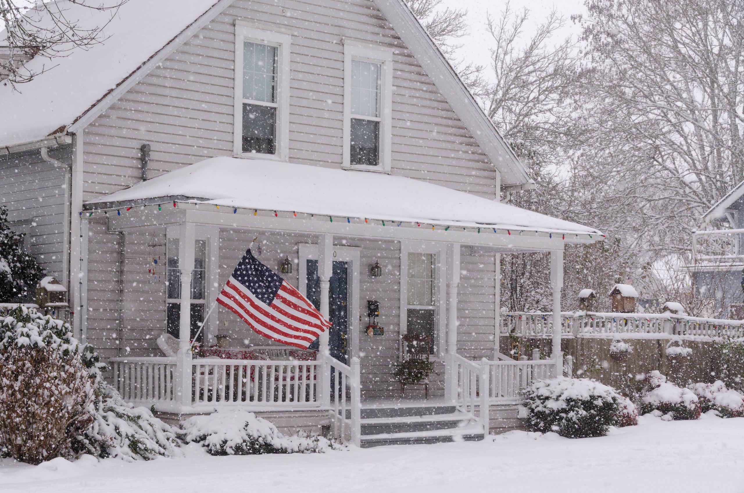 A house with an American flag while snow falls